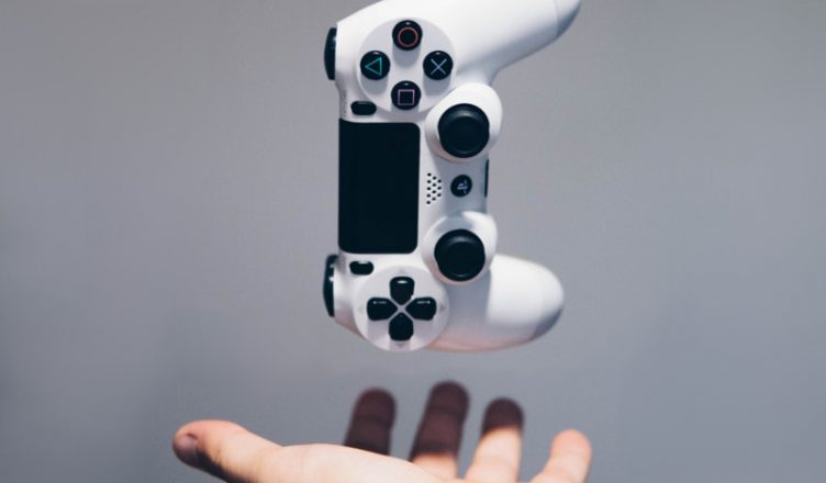 controlador ps4 blanco en el aire con una mano debajo en un fondo gris